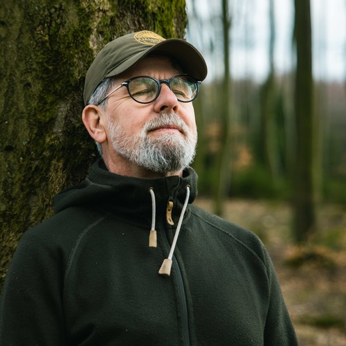 Ein Mann mit Mütze atmet an einem Baum tief durch.