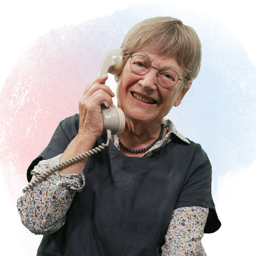 Eine ältere Frau hält lächelnd einen Telefonhörer an ihr Ohr